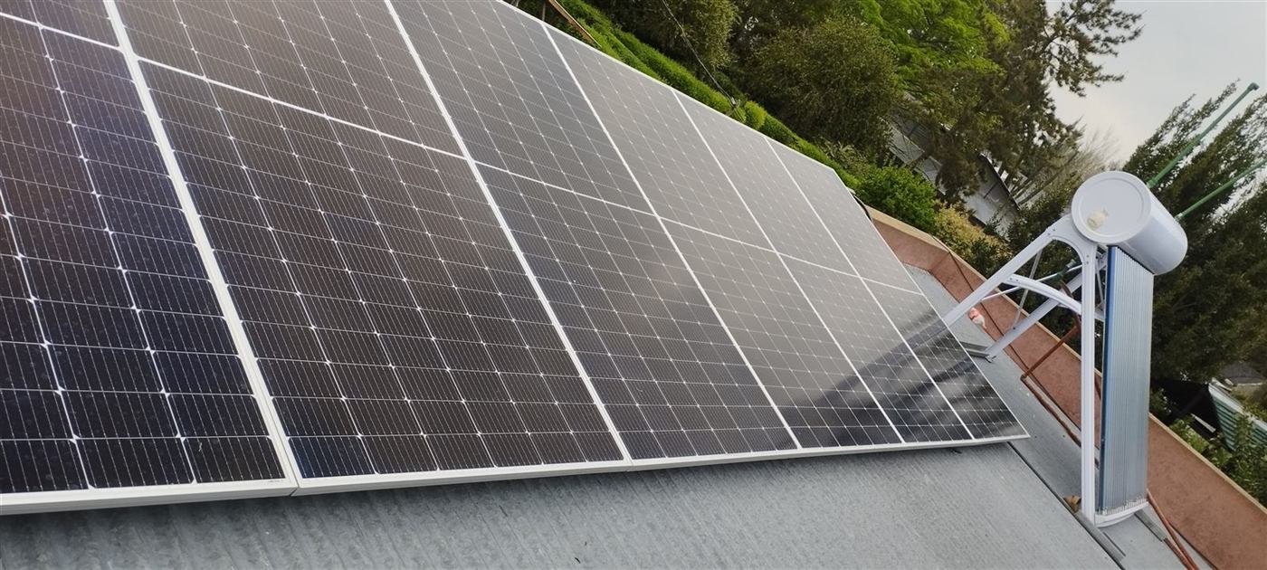 Paneles solares con montaje coplanar sobre techo de chapa, junto a un termotanque solar